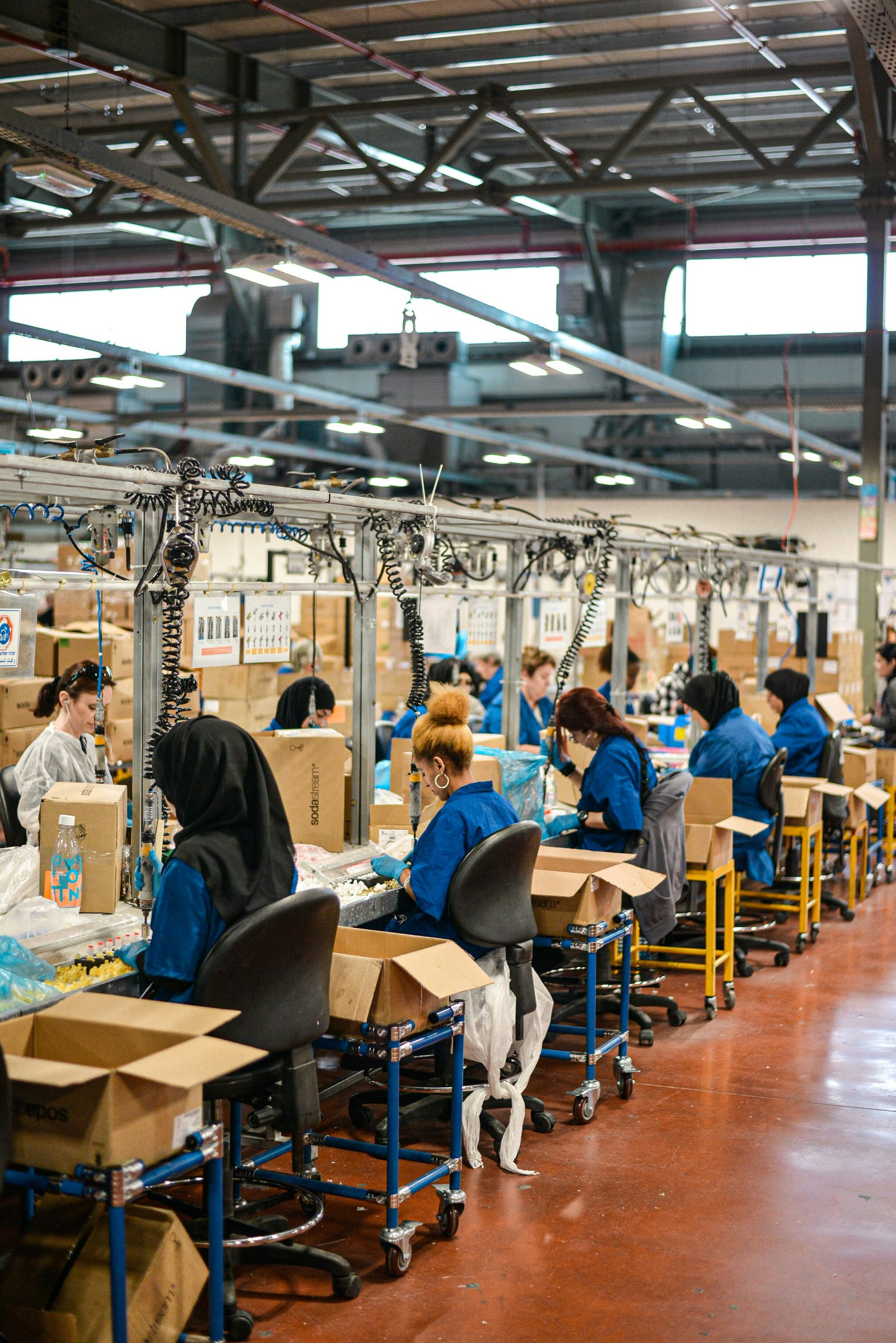 Linha de produção industrial com trabalhadoras realizando tarefas repetitivas em postos de trabalho